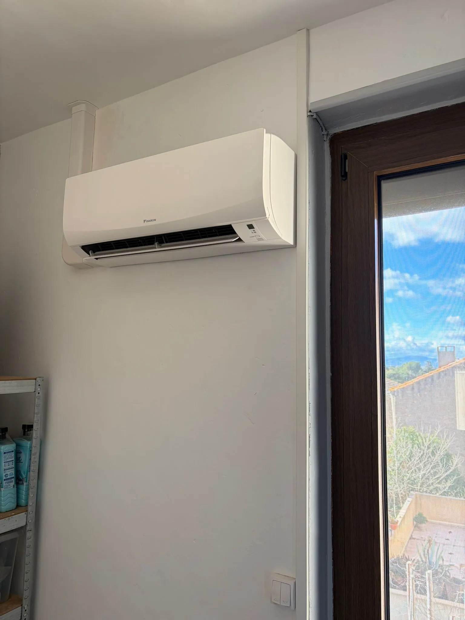 Unité murale Daikin blanche installée près d’une fenêtre, avec goulotte blanche