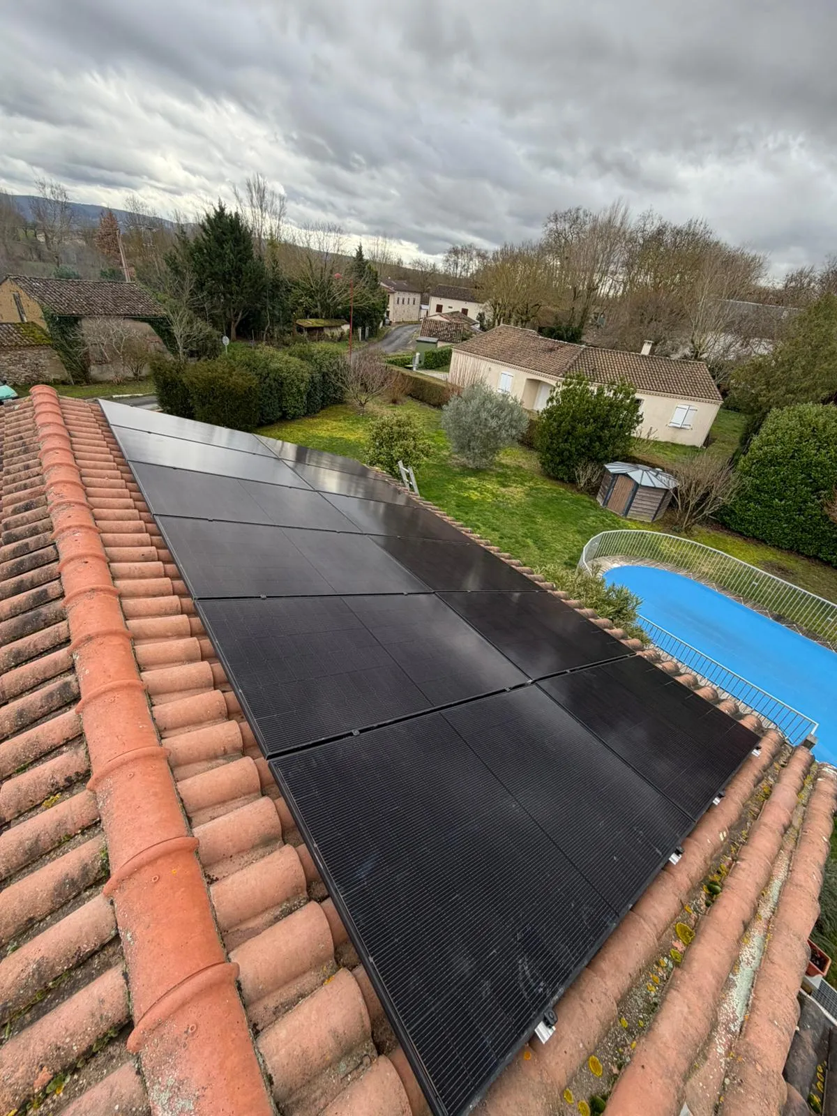 Panneaux photovoltaïques noirs sur un toit de tuiles rouges, avec jardin et piscine en contrebas