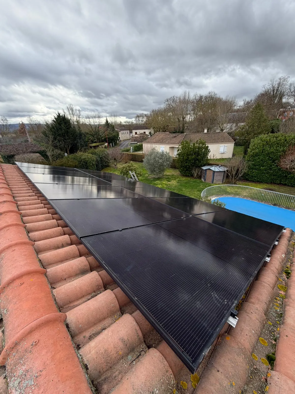 Panneaux photovoltaïques noirs sur un toit de tuiles rouges, avec jardin et piscine en contrebas