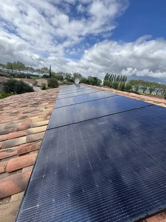 Panneaux photovoltaïques noirs installés sur une toiture en tuiles sous un ciel nuageux